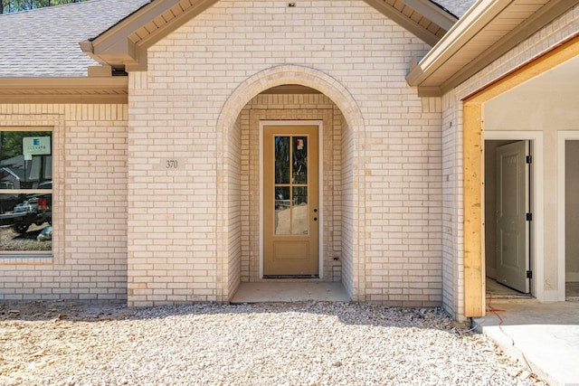 property entrance with roof with shingles and brick siding