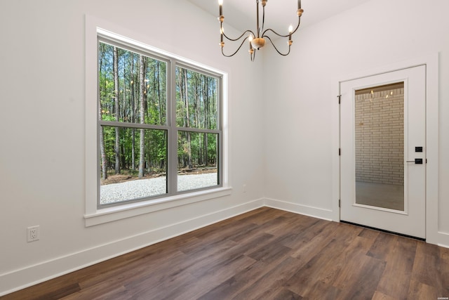 empty room featuring an inviting chandelier, dark wood-style flooring, and baseboards
