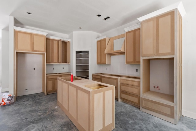 kitchen with concrete flooring, light brown cabinets, a kitchen island with sink, and under cabinet range hood