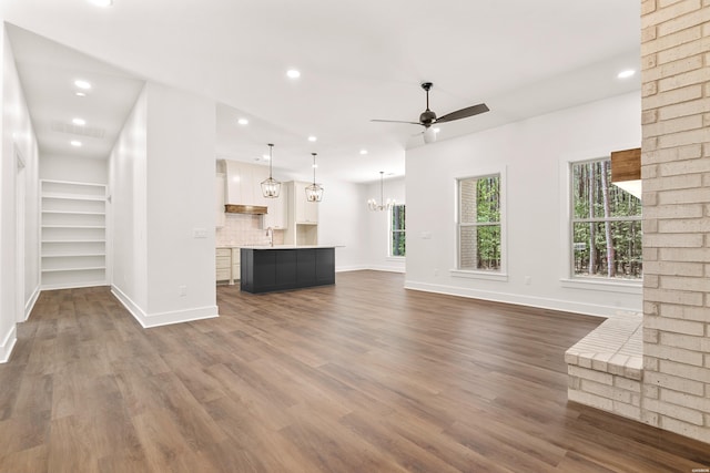 unfurnished living room with plenty of natural light, baseboards, and ceiling fan with notable chandelier