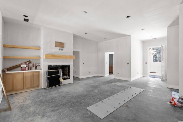 unfurnished living room featuring concrete flooring, a fireplace, and baseboards