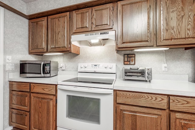 kitchen with brown cabinets, white electric range oven, light countertops, stainless steel microwave, and under cabinet range hood