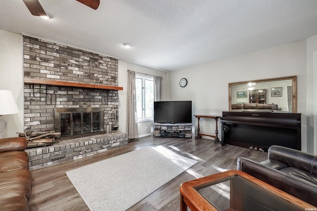 living area featuring a brick fireplace, a textured ceiling, baseboards, and wood finished floors