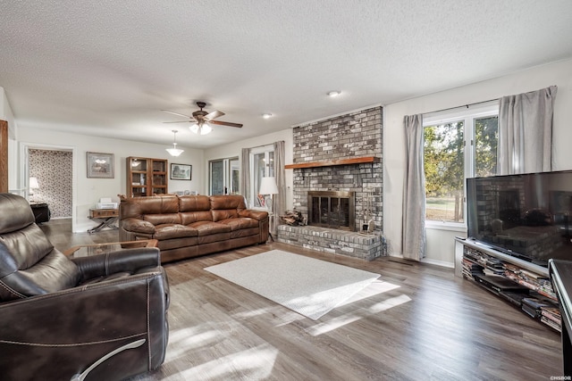 living room with a textured ceiling, wood finished floors, a ceiling fan, baseboards, and a brick fireplace