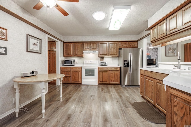 kitchen featuring light wood finished floors, light countertops, appliances with stainless steel finishes, brown cabinetry, and a sink