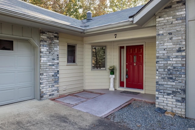 entrance to property featuring a shingled roof, brick siding, and an attached garage