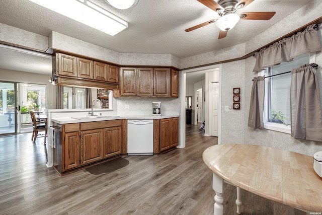 kitchen with brown cabinetry, light countertops, dishwasher, and a sink