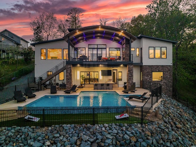 back of house at dusk with a patio area, stone siding, stairs, and fence