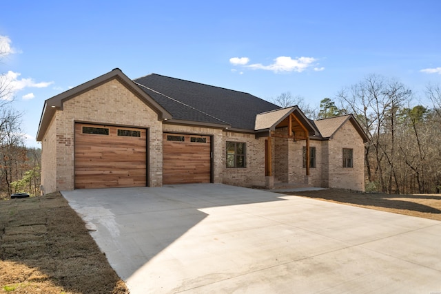 view of front of house featuring brick siding, driveway, an attached garage, and roof with shingles