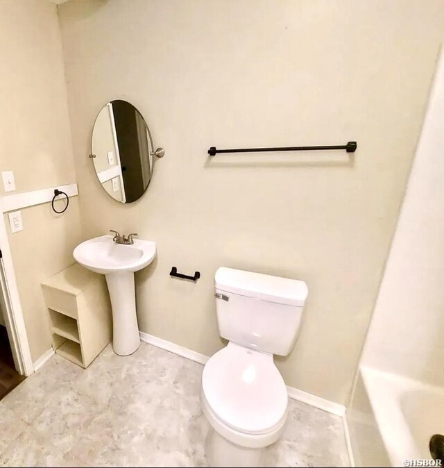 bathroom with baseboards, toilet, and a bath