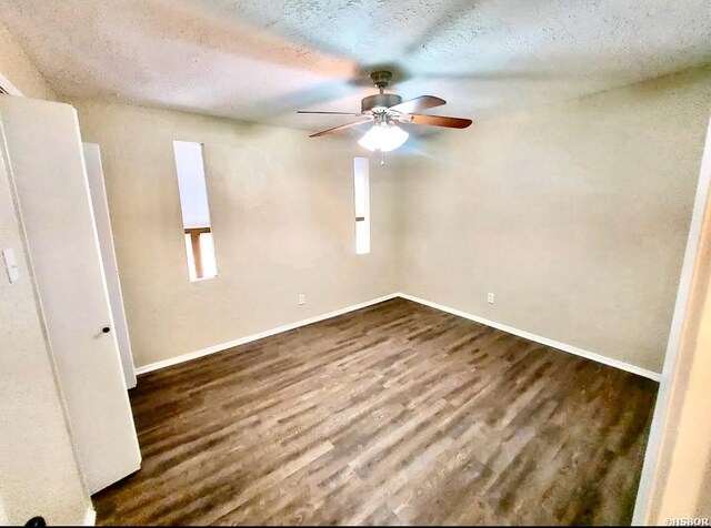 empty room with a textured ceiling, dark wood finished floors, a ceiling fan, and baseboards