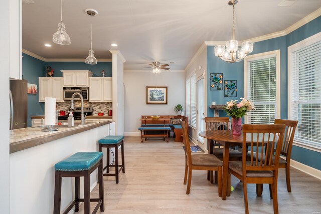 dining area with light wood-style floors, a ceiling fan, baseboards, and crown molding