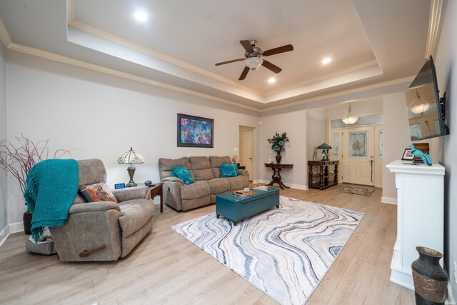 living room featuring light wood-style floors, a tray ceiling, crown molding, and baseboards