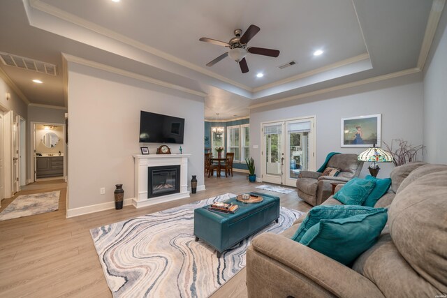 living area featuring light wood finished floors, a tray ceiling, visible vents, and baseboards