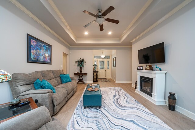 living area with a ceiling fan, baseboards, light wood-style floors, a raised ceiling, and crown molding