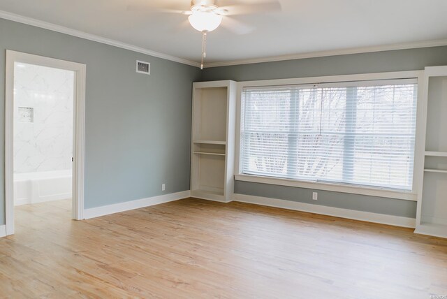 spare room featuring light wood finished floors, plenty of natural light, visible vents, and crown molding