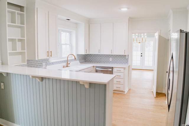 kitchen featuring white cabinets, a peninsula, stainless steel appliances, light countertops, and a sink