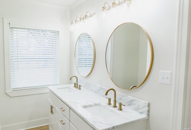 full bath featuring double vanity, ornamental molding, a sink, and baseboards