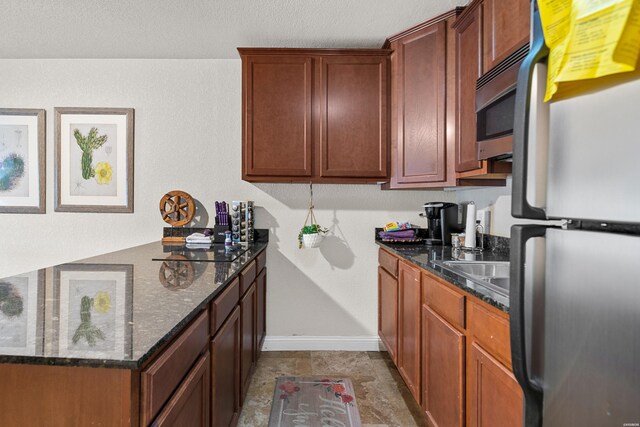 kitchen featuring appliances with stainless steel finishes, dark stone counters, brown cabinets, and baseboards