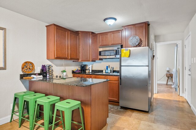 kitchen featuring brown cabinets, appliances with stainless steel finishes, dark stone countertops, a peninsula, and a kitchen breakfast bar