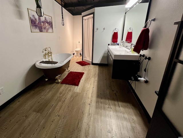 bathroom with baseboards, toilet, a soaking tub, wood finished floors, and vanity