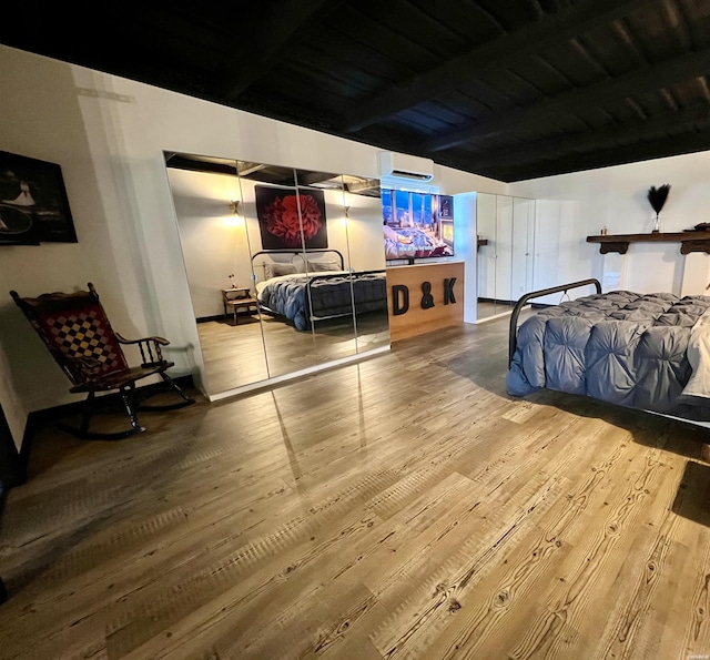 bedroom with beam ceiling, wood finished floors, and a wall mounted AC