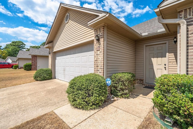 doorway to property with concrete driveway, brick siding, roof with shingles, and an attached garage