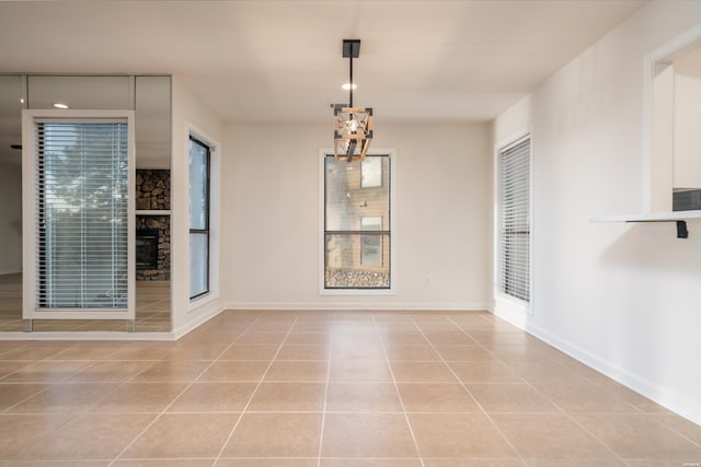 unfurnished dining area with light tile patterned floors, a stone fireplace, and baseboards