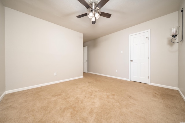 spare room featuring light carpet, ceiling fan, and baseboards