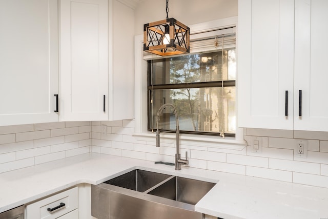 kitchen featuring light stone counters, a sink, white cabinetry, and decorative backsplash