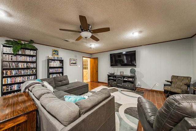 living room featuring ceiling fan, a textured ceiling, wood finished floors, visible vents, and crown molding