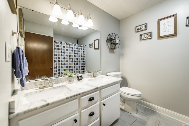 full bathroom featuring a textured ceiling, double vanity, a sink, and toilet