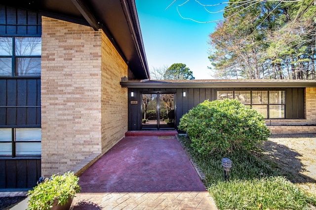 property entrance with french doors, board and batten siding, and brick siding