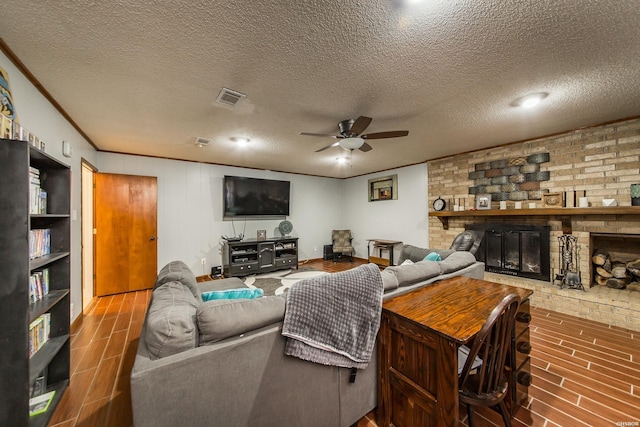 living room with wood finish floors, visible vents, ornamental molding, a brick fireplace, and a textured ceiling