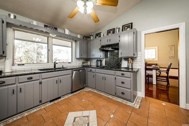 kitchen featuring gray cabinets, backsplash, stainless steel dishwasher, a sink, and under cabinet range hood