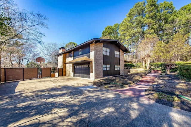 view of property exterior featuring a garage, concrete driveway, a chimney, fence, and brick siding