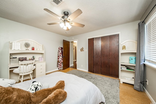 bedroom with a textured ceiling, ceiling fan, visible vents, baseboards, and a closet