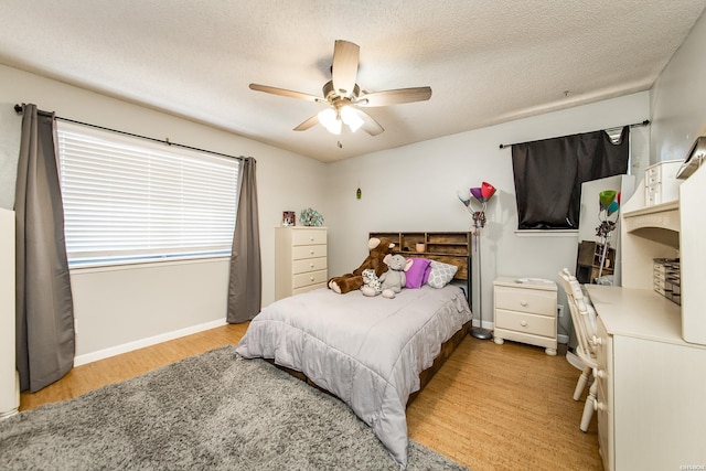 bedroom with a textured ceiling, ceiling fan, light wood-style flooring, and baseboards