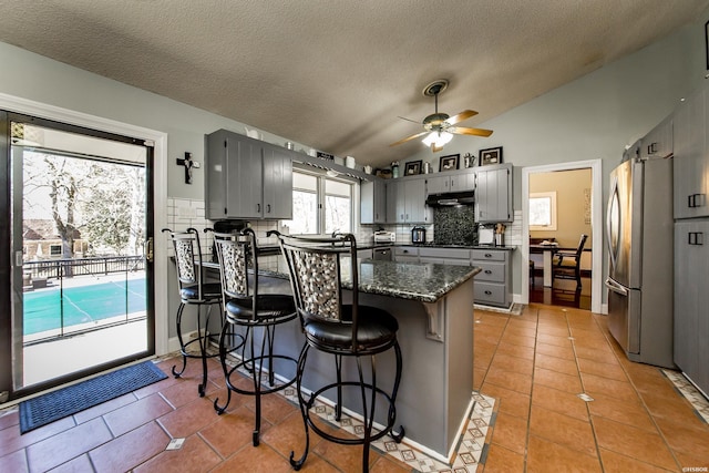 kitchen with a peninsula, light tile patterned flooring, gray cabinets, and freestanding refrigerator