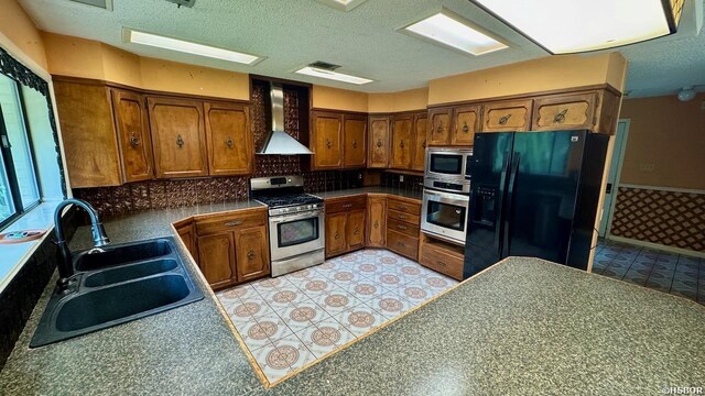 kitchen with a sink, appliances with stainless steel finishes, wall chimney range hood, light floors, and dark countertops