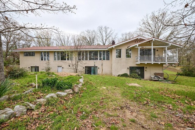 back of house featuring a balcony, stucco siding, a chimney, and a yard