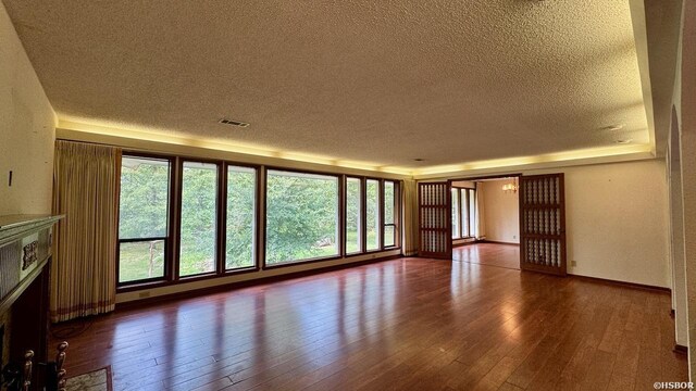 unfurnished living room with a fireplace with flush hearth, visible vents, a textured ceiling, and wood finished floors