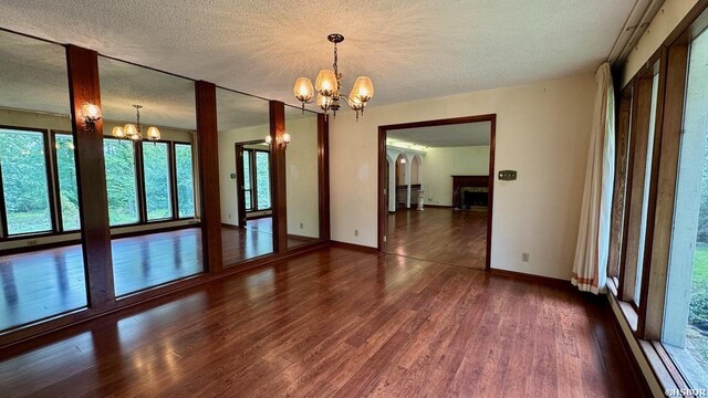 unfurnished room featuring dark wood-style floors, a fireplace, a notable chandelier, a textured ceiling, and baseboards