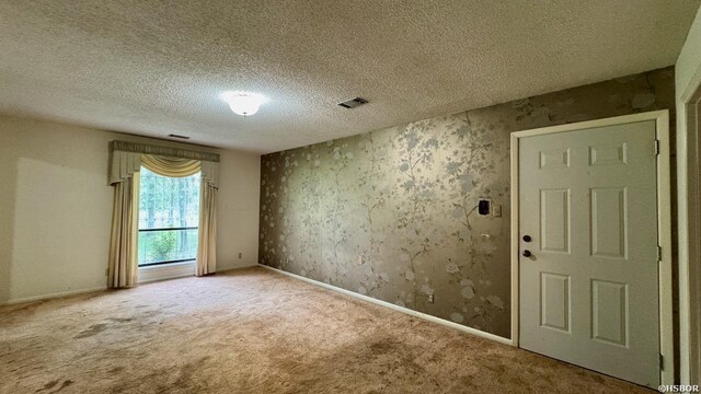 carpeted spare room featuring baseboards, visible vents, and a textured ceiling