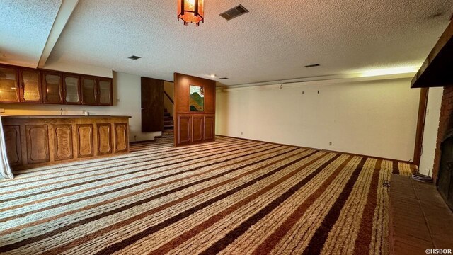 unfurnished living room with light carpet, stairway, a textured ceiling, and visible vents