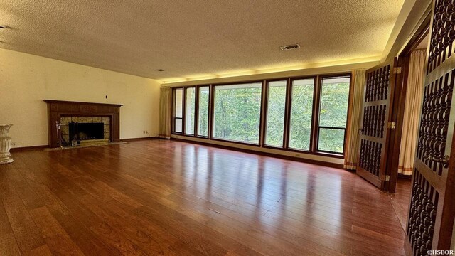 unfurnished living room featuring a high end fireplace, visible vents, a textured ceiling, and wood finished floors