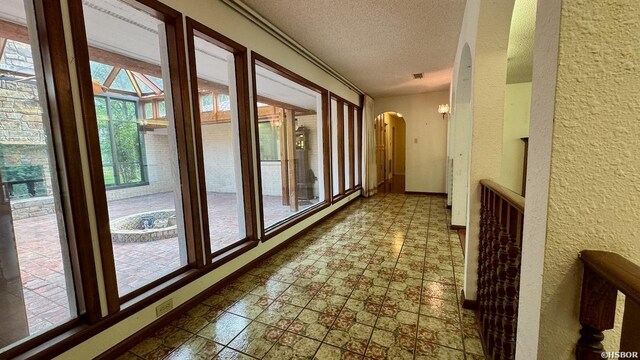 hallway with arched walkways, a textured wall, a textured ceiling, and baseboards