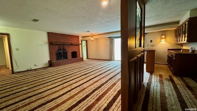 carpeted living area with a textured ceiling, a fireplace, visible vents, and a sink