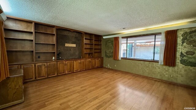 unfurnished living room featuring visible vents, light wood-style flooring, and a textured ceiling