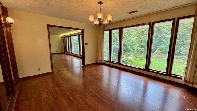 unfurnished room featuring plenty of natural light, visible vents, dark wood finished floors, and an inviting chandelier